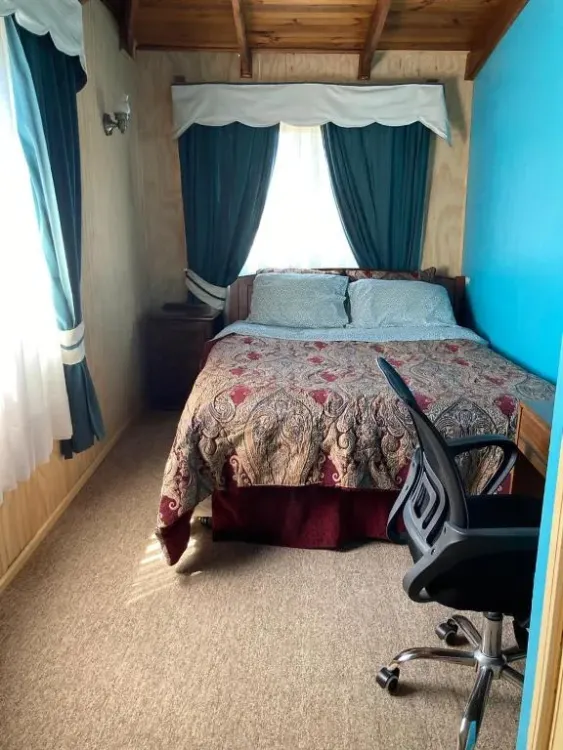 Dormitorio con cama matrimonial, cortinas y silla de escritorio
